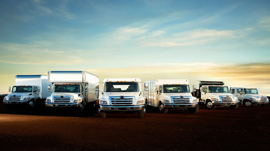 a commercial fleet of new work trucks is lined up on the road before a sunset